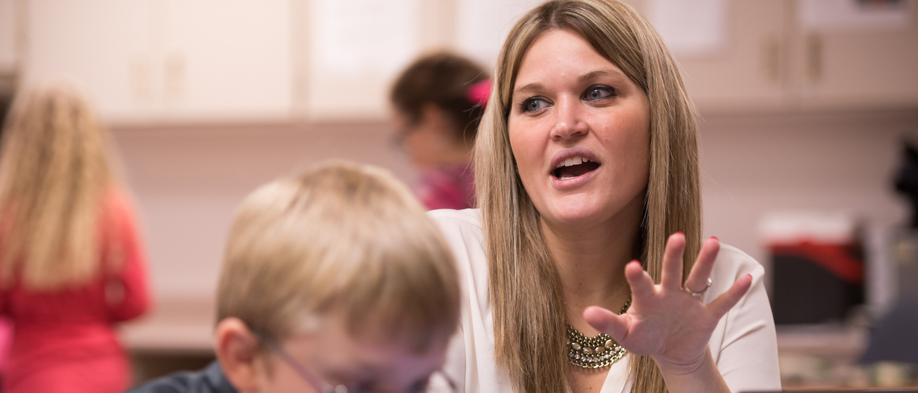 Person gesturing in a classroom with young children.